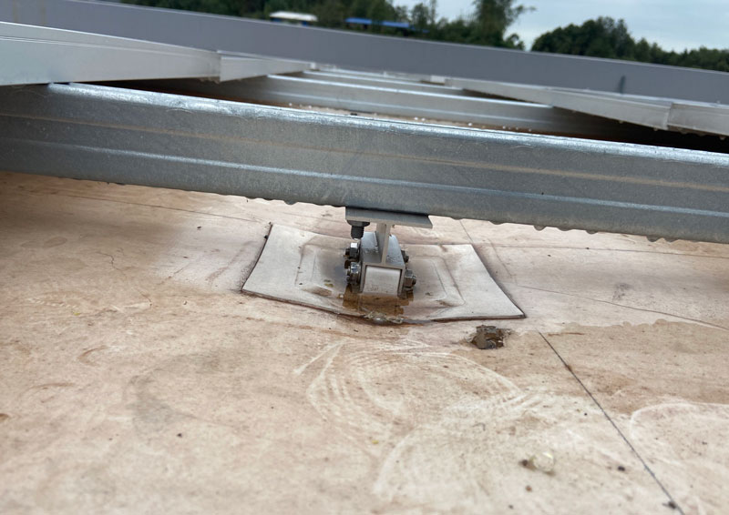Traditional tpo roof base depression - Valin New Energy Close-up of a rooftop solar mounting rail supported by a pedestal on a flat concrete roof, with sealant around the base